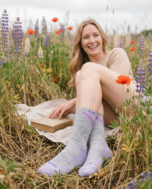 Lifestyle (woman in wildflower field) → "Woman smiling in a wildflower field wearing Climatesox.com E-Zmate Women's Linkable Merino Wool Crew Socks